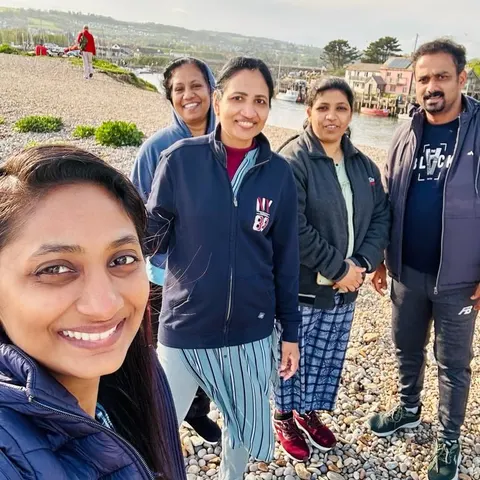 Five people taking a selfie on a pebble beach by a harbour