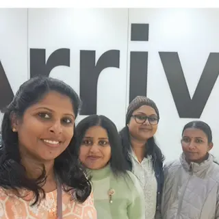 Four women smiling under an arrivals sign