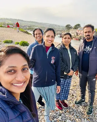 Five people taking a selfie on a pebble beach by a harbour